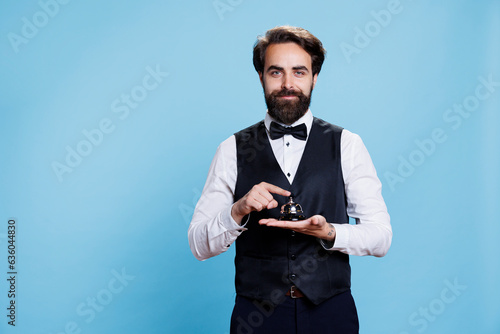 Hotel concierge holds service bell used to ring for assistance and help at front desk. Male bellboy empoyee in formal suit presenting hospitality industry, doorkeeper porter job.