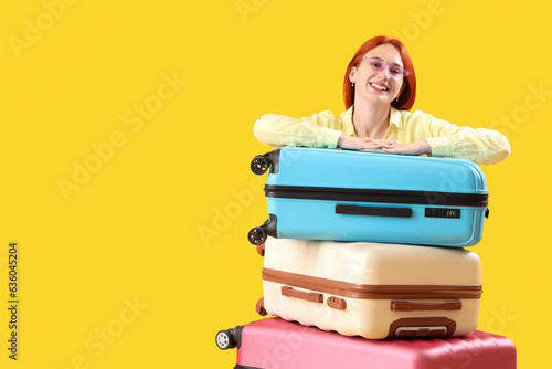 Female tourist with suitcases on yellow background