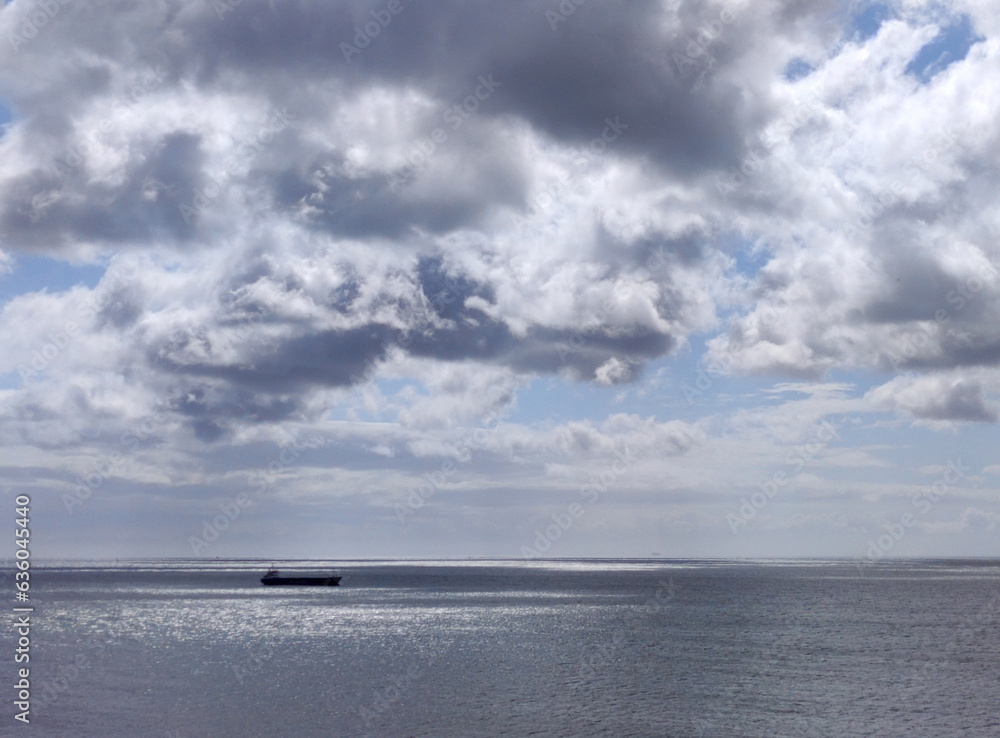 Cargo ship in the open sea. White clouds over a stormy sky background and sea