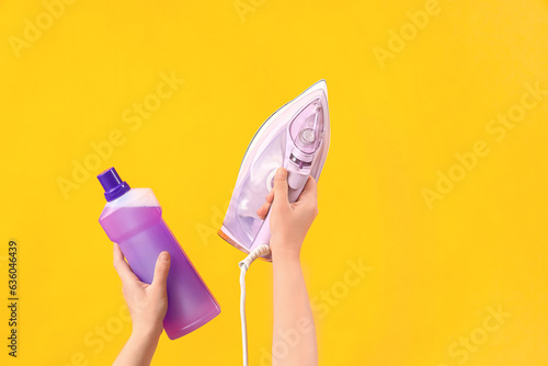 Woman with bottle of laundry detergent and iron on yellow background