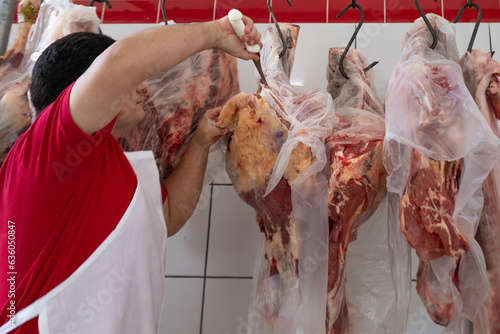 Man cutting a carcass hanging from the hooks at butchery photo