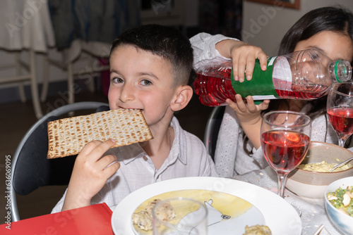 Funny Jewish boy sits at the table, biting off a piece of matzah.
 photo