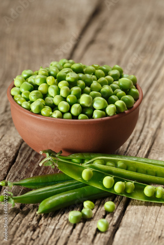 Green peas in closed and open pods, peeled peas in a bowl, scattered pea seeds on a wooden background.