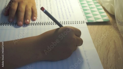 Kid's hands close up writing in copybook on wooden desk under lamp. 10-12 years old child doing homework. High quality HD footage photo