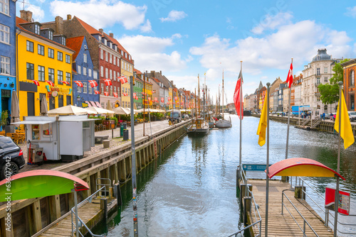Colorful buildings with apartments  and shops alongside outdoor sidewalk cafes and docked sailboats at the 17th century Nyhavn Canal  a major tourist destination in the city of Copenhagen  Denmark.