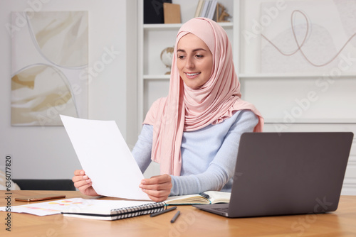 Muslim woman working near laptop at wooden table in room