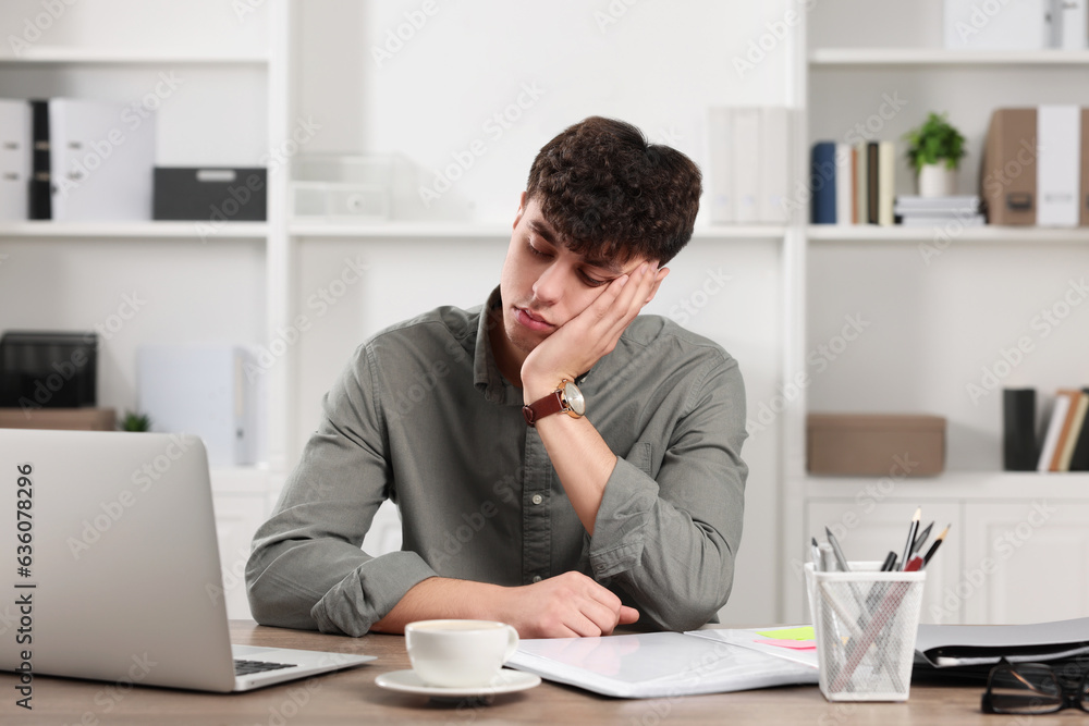 Tired young man working at table in office. Deadline concept Tired young man working at table in office. Deadline concept