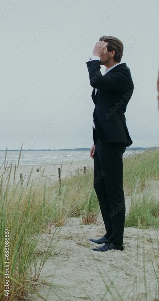 A man in formal clothes straightens his hair standing on the seashore and looking into the distance with a serious face A man in formal clothes straightens his hair standing on the seashore and looking into the distance with a serious face