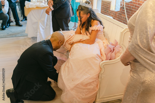 father putting shoe on teenage girl celebrating quinceanera photo