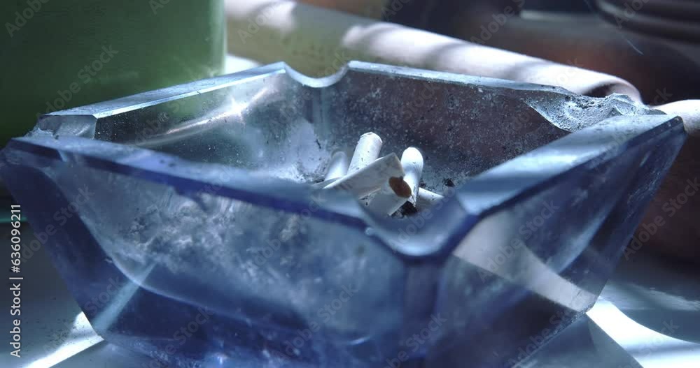Close up of a hand with a cigarette knocking the ash off and then tipping the cigarette into the ashtray Close up of a hand with a cigarette knocking the ash off and then tipping the cigarette into the ashtray