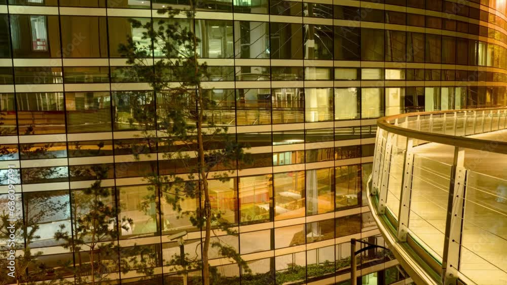 Timelapse reveals a modern building at night with a curved glass facade reflecting the orange glow from the street lights and a balcony with glass railing Timelapse reveals a modern building at night with a curved glass facade reflecting the orange glow from the street lights and a balcony with glass railing