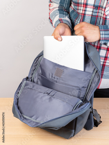 The hands of an unrecognizably cropped man in a plaid shirt put a laptop in a backpack, going to work. photo