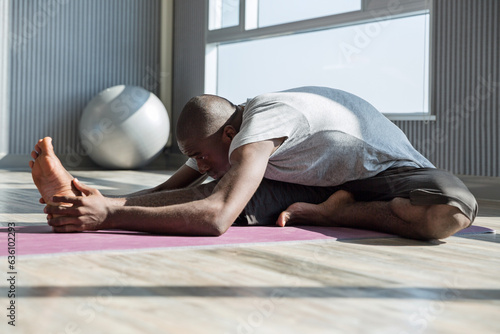 Man practicing janusirsasana yoga pose with one knee bent out to side photo