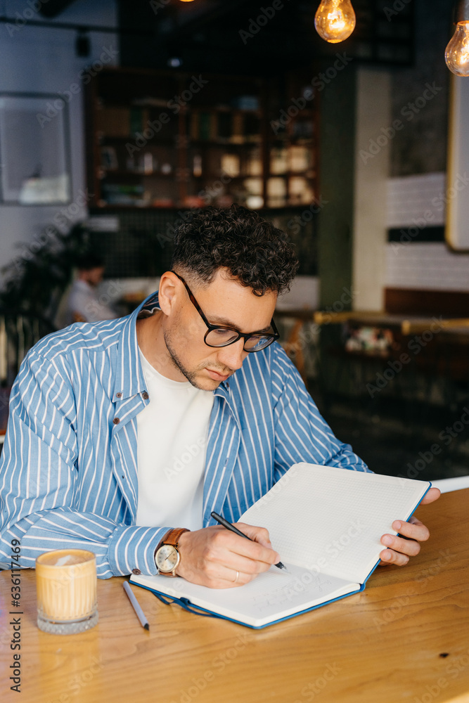 A man writes in his notebook while sitting in a cafe A man writes in his notebook while sitting in a cafe