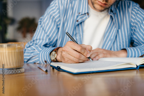 A man writes in a notebook while sitting indoors photo