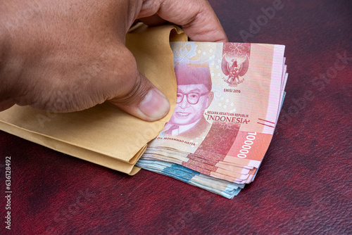 row of Indonesian rupiah banknotes in a salary envelope, on a brown and maroon leather sova photo