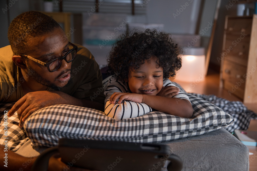 Curious dad with little son using digital tablet lying on bed at home ...
