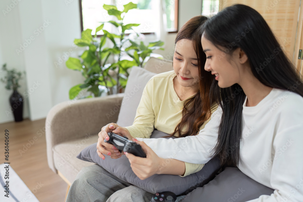 Asian beautiful lesbian gay couple enjoy play game together in Livingroom. Two female friend sit on sofa in living room, feel happy to play joystick game at home. Asian beautiful lesbian gay couple enjoy play game together in Livingroom. Two female friend sit on sofa in living room, feel happy to play joystick game at home.