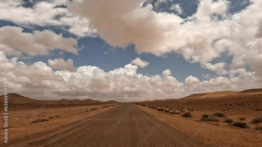 Driving on desert road along arid landscape with white clouds in blue sky. First-person driver point of view Driving on desert road along arid landscape with white clouds in blue sky. First-person driver point of view
