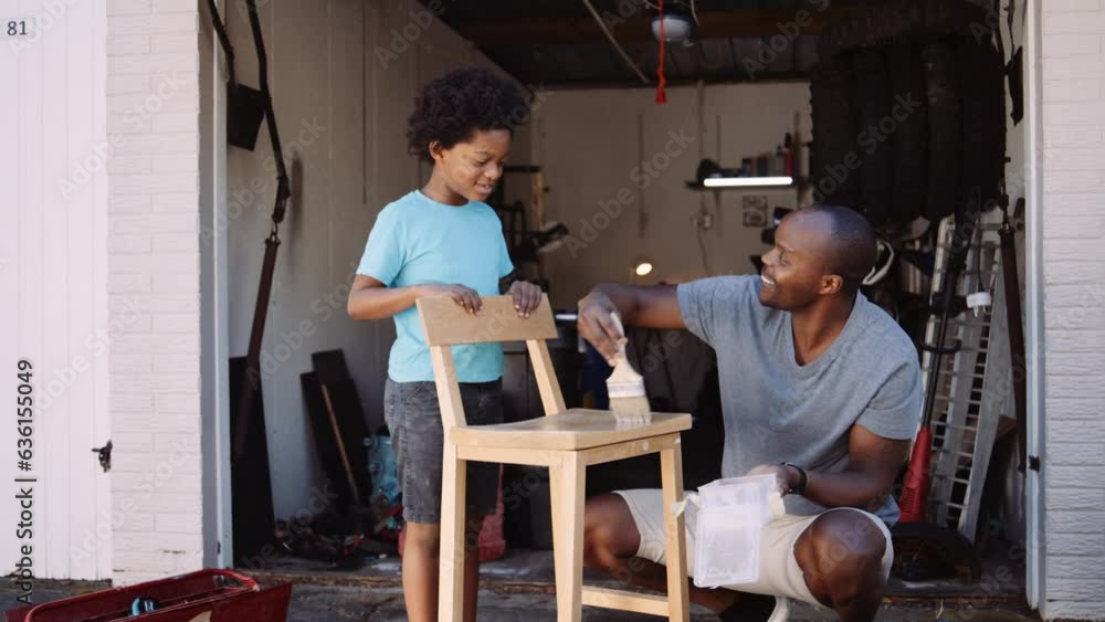 Mixed race father teaching son how to varnish the wooden chair at home during DIY project in the garage Mixed race father teaching son how to varnish the wooden chair at home during DIY project in the garage