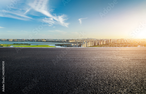 Asphalt road and urban skyline with lake at sunset
