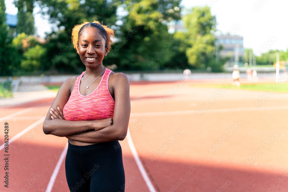 A confident black woman, dressed in athletic attire, strikes a pose with crossed arms and a beaming smile, exuding joy and radiance. Her vibrant energy shines through as she embraces her sporty style.