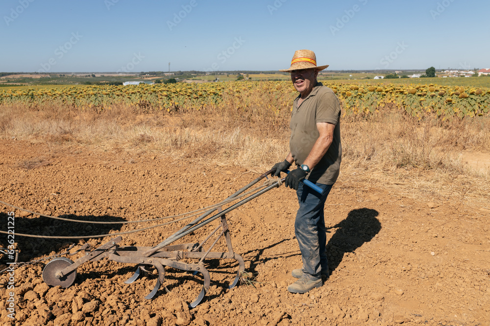 Smiling male farmer plowing soily field manually in countryside Smiling male farmer plowing soily field manually in countryside