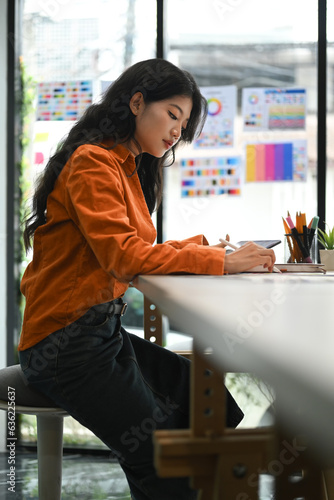 Concentrated young creative woman sitting in bright office and working on design project. photo