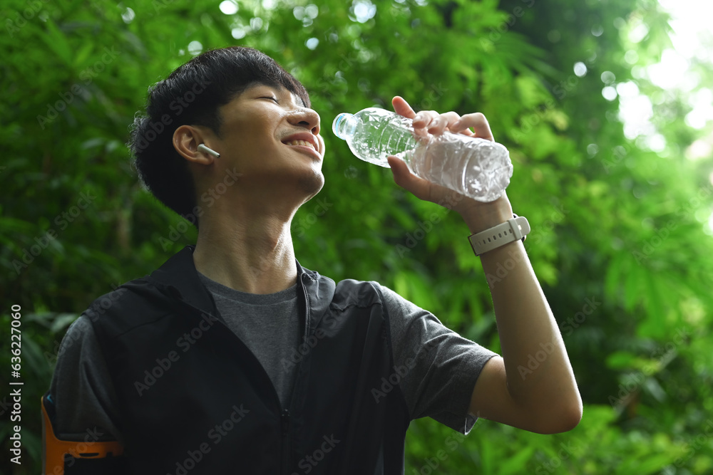 Delighted male runner drinking water from a bottle relaxing after resting after trail running. Delighted male runner drinking water from a bottle relaxing after resting after trail running.