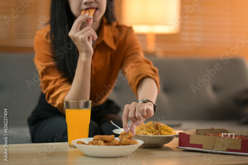 Shot of young woman enjoying pizza while sitting on couch in cozy living room. People and food concept.