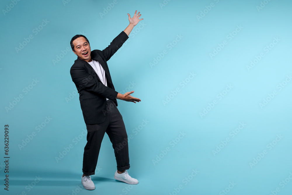 Full length portrait of happy smiling Asian businessman presenting to the side over blue background Full length portrait of happy smiling Asian businessman presenting to the side over blue background
