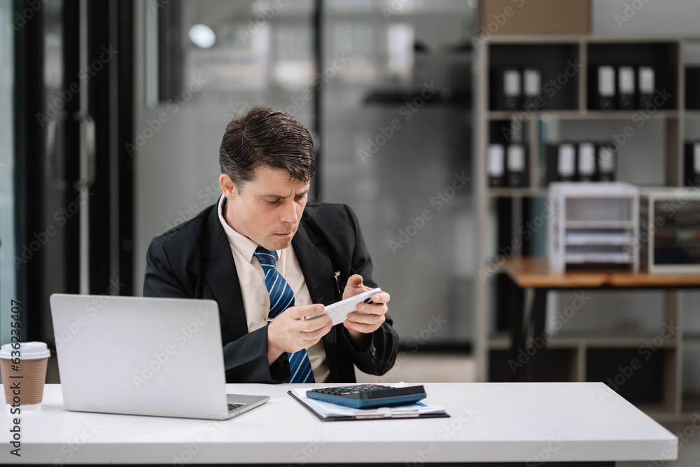 Happy young man looking at cellphone screen, reading message, or email, communicating distantly with client or playing games from computer work in modern office. Happy young man looking at cellphone screen, reading message, or email, communicating distantly with client or playing games from computer work in modern office.
