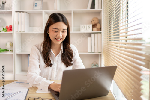 Woman using laptop to work or do homework at home with smiling face in her office, Creating happiness at work with a smile, Live performance or vdo call with laptop, Work from home.