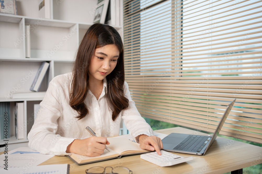 Beautiful young asian woman watching live video or video call of teacher teaching on laptop in her home, Take notes of important conversations and messages during the teacher's teaching. Beautiful young asian woman watching live video or video call of teacher teaching on laptop in her home, Take notes of important conversations and messages during the teacher's teaching.