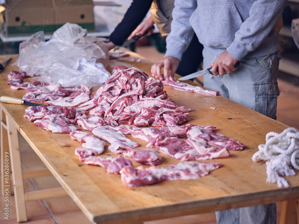 Crop male farmers cutting raw meat on wooden table in butchery