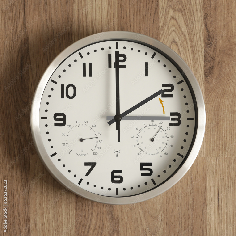 A clock, the gray hand points to three o'clock, the black one to two o'clock. The orange arrow indicates the direction of movement of the hands. Symbol of the time change. Standard time. A clock, the gray hand points to three o'clock, the black one to two o'clock. The orange arrow indicates the direction of movement of the hands. Symbol of the time change. Standard time.