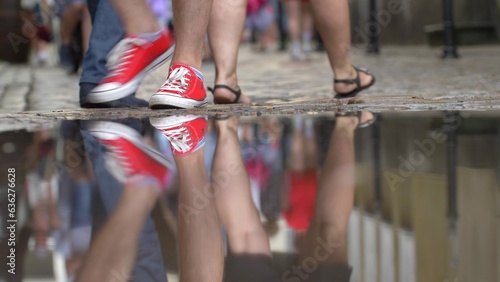 Anonymous Crowd Legs Walking on Cobblestone Street Reflected in Puddle