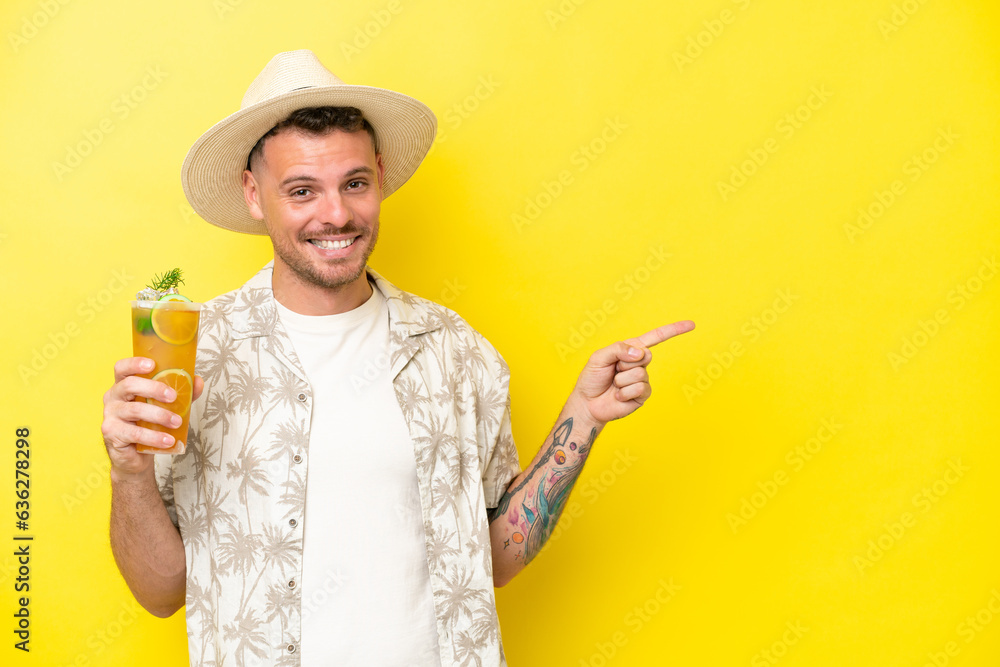 Young caucasian man holding a cocktail isolated on yellow background pointing finger to the side Young caucasian man holding a cocktail isolated on yellow background pointing finger to the side