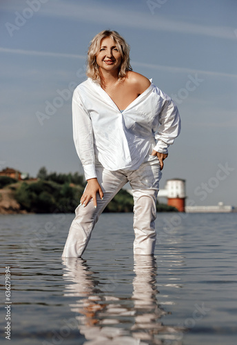 portrait beautiful middle-aged woman in white shirt and trousers on the seashore, concept of youth in adulthood