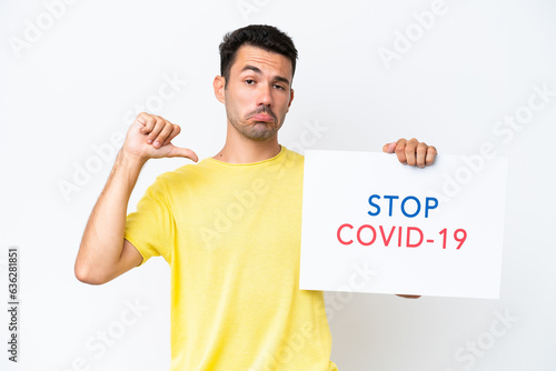 Young handsome man over isolated white background holding a placard with text Stop Covid 19 with proud gesture © luismolinero