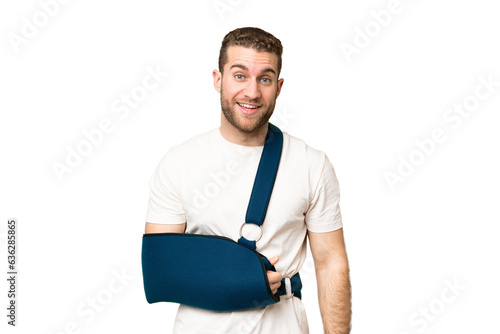 Young handsome blonde man with broken arm and wearing a sling over isolated chroma key background with surprise facial expression