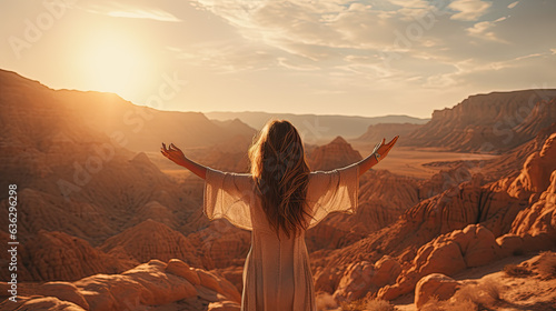 a young pretty woman with long hair stretches her arms up to the sides in front of a desert and looks into the distance.
