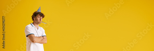 Unpleasant and unhappy mature man celebrating his birthday agsisnt yellow studio background. Concept of human emotions, facial expression, lifestyle, holidays. Banner. Copy space for ad
