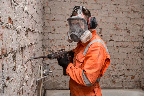Construction  worker wearing full face respirator mask and ear defenders for working with hammer drill.