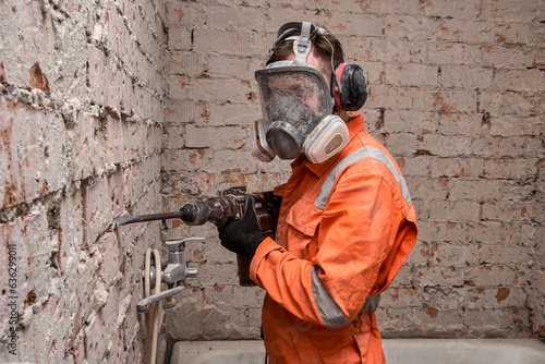 Construction  worker wearing full face respirator mask and ear defenders for working with hammer drill. photo
