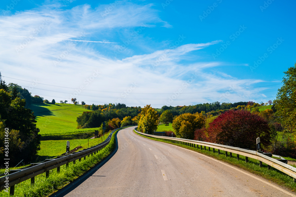 Germany, colorful trees alongside curved road in autumn with blue sky at sunrise romantic atmosphere hiking