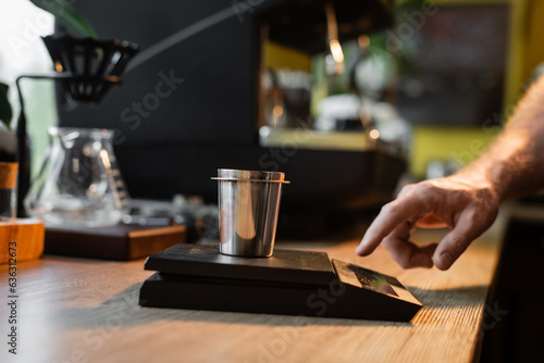 cropped view of barista using electronic scales and beaker near blurred coffee machine in cafe