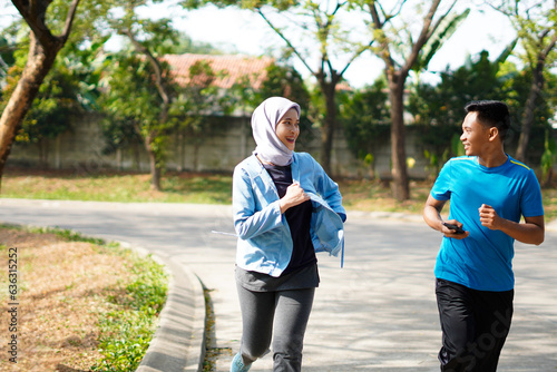 Young muslim couple happy together running at green summer park. Man and woman in hijab doing morning workout outdoors. photo
