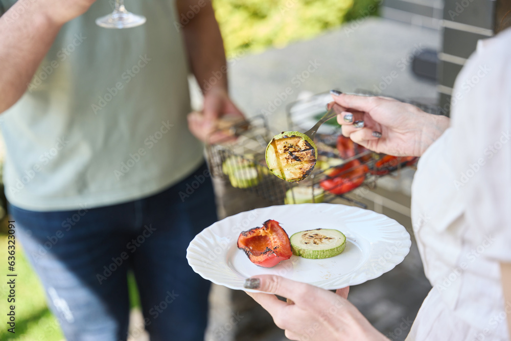 Woman stands with a plate of grilled vegetables in backyard