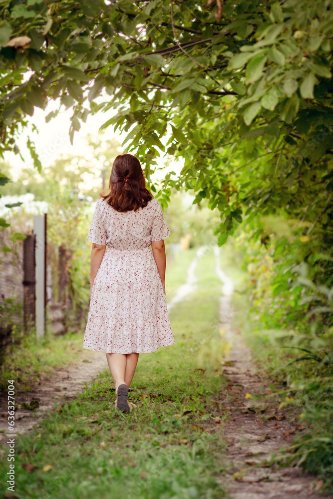 romantic young woman walks in nature, view of a girl in a summer dress from the back romantic young woman walks in nature, view of a girl in a summer dress from the back